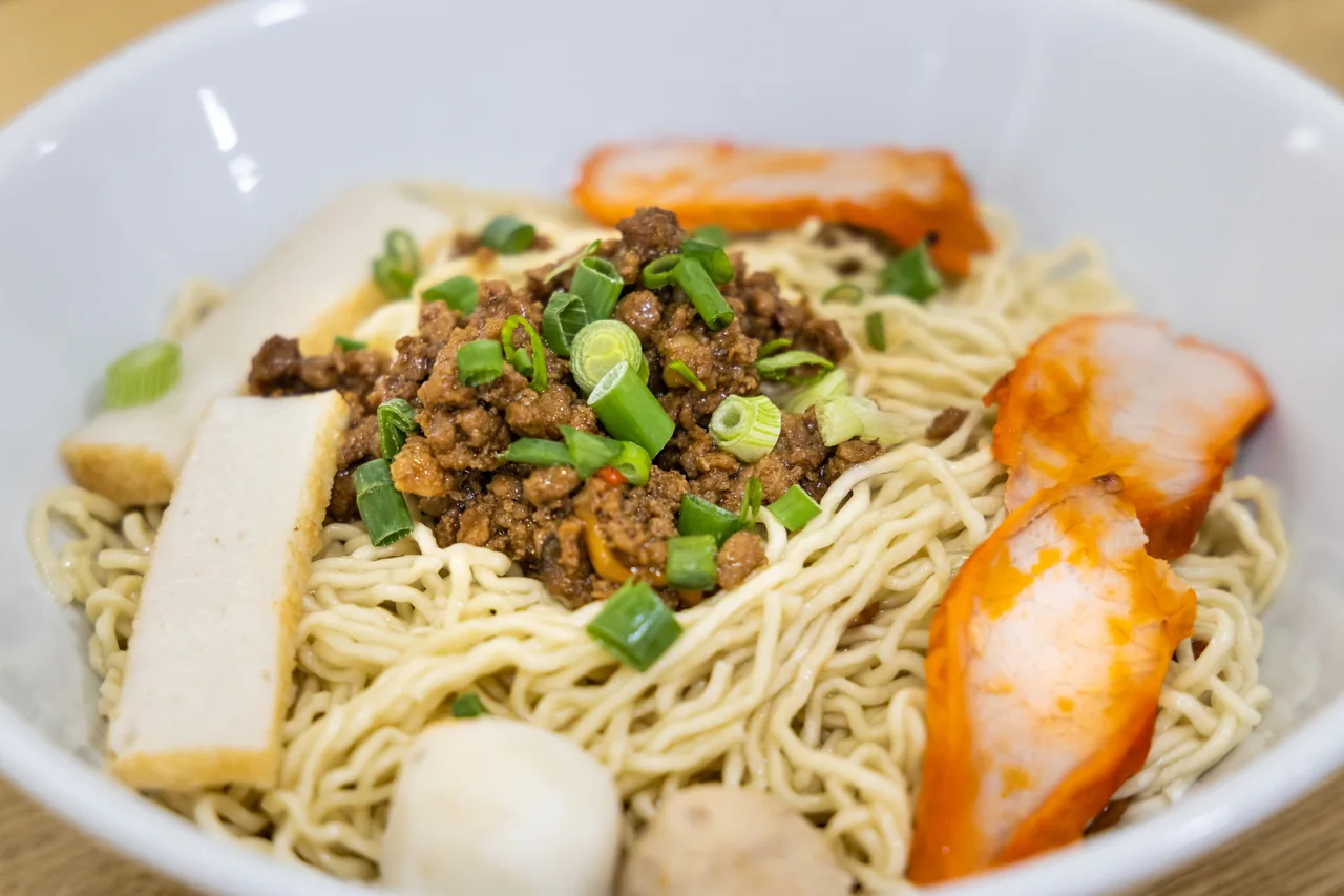 A bowl of kolo mee with noodles and toppings